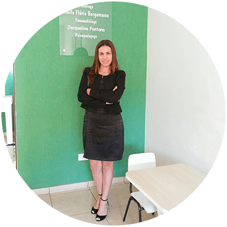 Psicologa Izabel Morais em pe com os bracos cruzados em uma parede verde